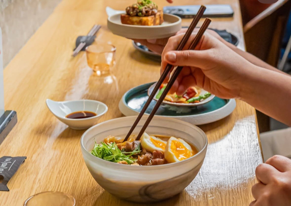 Comensal usando palillos frente a un tazón con huevo y diversos platillos japoneses en la barra de Tokoya.